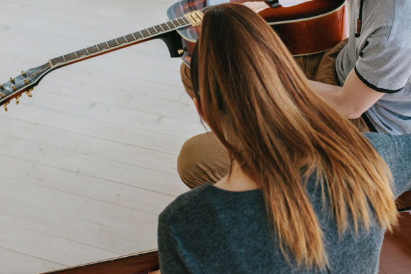 Frau von hinten zu sehen, bekommt Gitarrenspielen erklärt